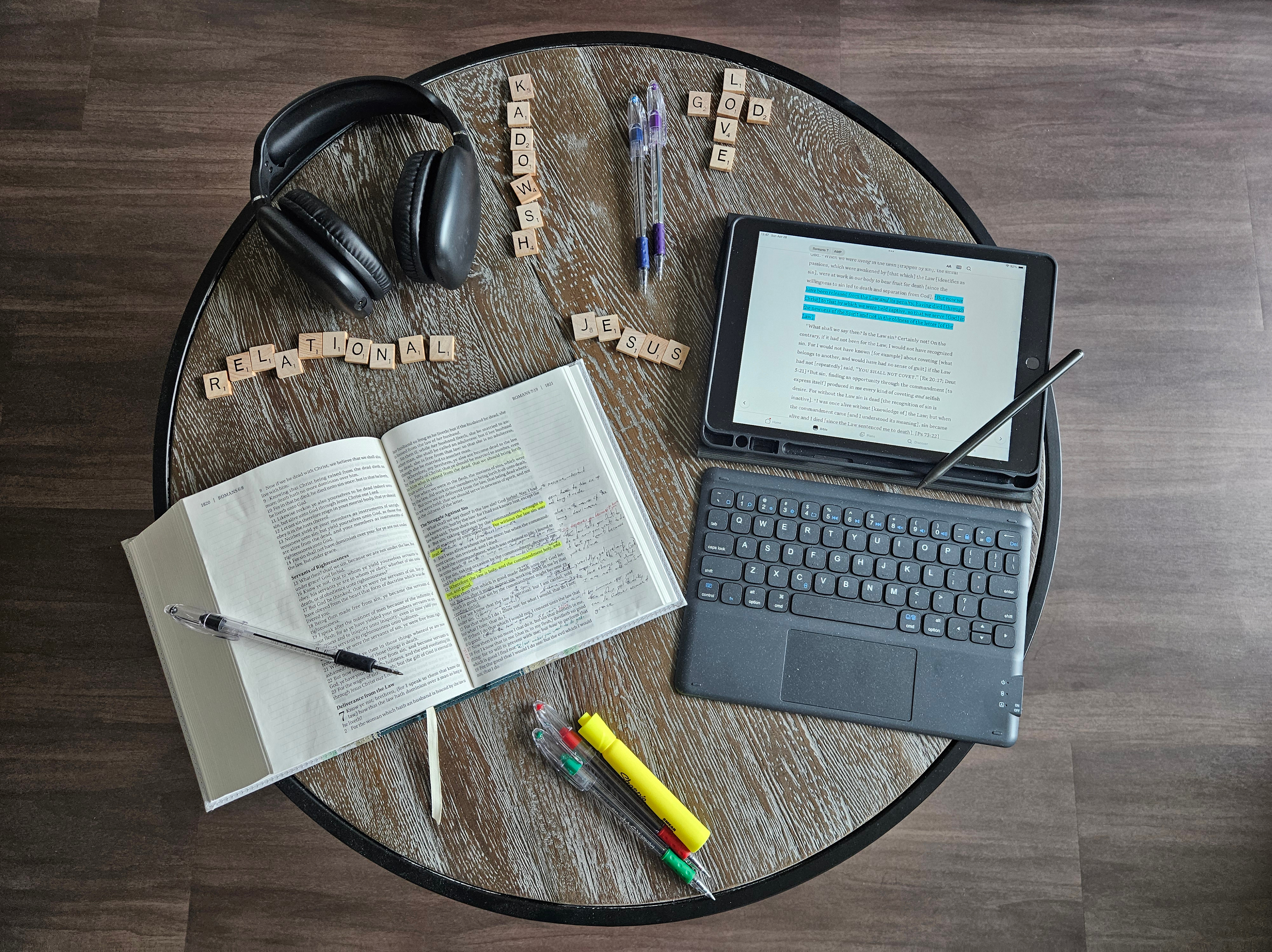 Headphones, pens, highlighters, scrabble tiles, open bible, and an iPad on a circular table
